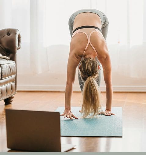 A woman is doing yoga in front of the laptop.