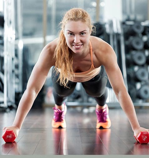 A woman is doing push ups with red dumbbells.