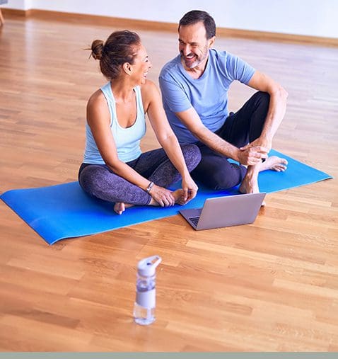 A man and woman sitting on the ground with a laptop.